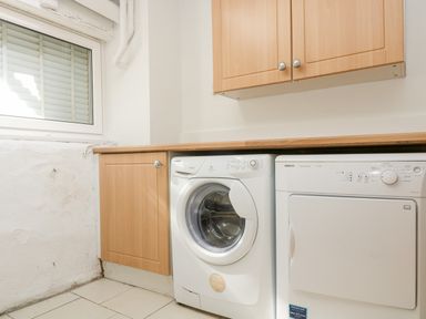 A laundry room with a washing machine and dryer under a wooden countertop and cabinet at Mallards in Pentewan