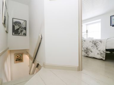 A staircase with framed pictures on the wall and a bedroom visible with a bed covered in a floral bedspread at Mallards in Pentewan