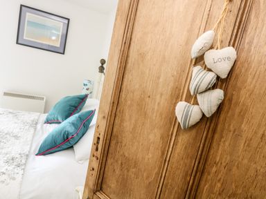 A bedroom with teal pillows on a bed and a wooden door with love heart decorations at Mallards in Pentewan