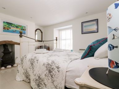 A bedroom with a metal bed frame and floral bedspread with folded towels on the bed a wood stove on the left and paintings on the walls at Mallards in Pentewan