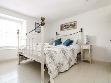 A bedroom with a white metal bed frame and floral bedspread with two teal pillows at Mallards in Pentewan