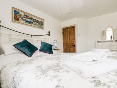 A bedroom with a bed with pillows and folded towels a wooden door a dresser with a mirror and a bedside table with a lamp at Mallards in Pentewan