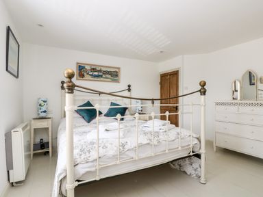 A bedroom with a metal bed frame two teal pillows a white dresser with mirrors and wooden door at Mallards in Pentewan