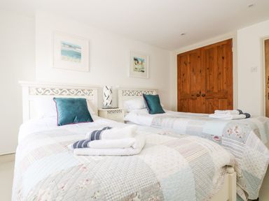 A bedroom with two single beds with patterned quilts and teal cushions and a wooden closet at Mallards in Pentewan
