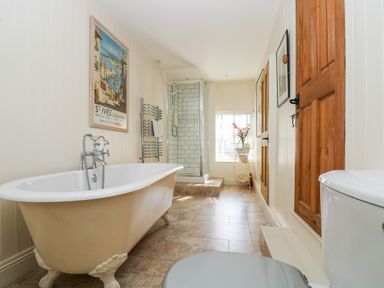 A bathroom with a freestanding bathtub shower cubicle wooden doors and a toilet at Mallards in Pentewan