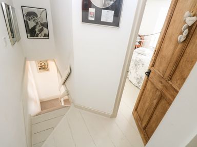 A staircase leading down with framed pictures on the walls and an open wooden door revealing a bedroom at Mallards in Pentewan