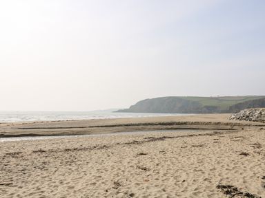 A sandy beach with a small water channel and a rocky hill in the background at Mallards in Pentewan