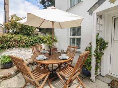 An outdoor patio with a round wooden table and four chairs under a white umbrella at Mallards in Pentewan