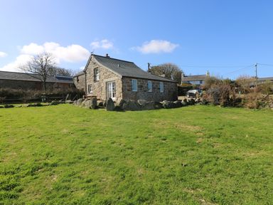 A stone house with a grass lawn and trees under a blue sky at Boar's House in Penzance