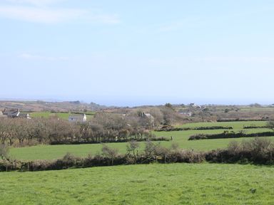 Green fields with hedgerows and houses under a blue sky at Boar's House in Penzance