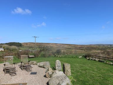 An outdoor area with two wooden chairs on gravel and grass with hills in the background at Boar's House in Penzance