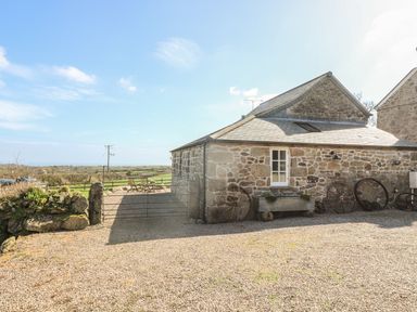 A stone building with old wagon wheels leaning against it and wooden chairs on a gravel area outside at Boar's House in Penzance