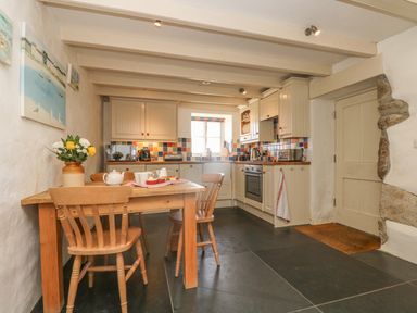 A kitchen with a wooden table and chairs a window above the sink and cabinets at Boar's House in Penzance