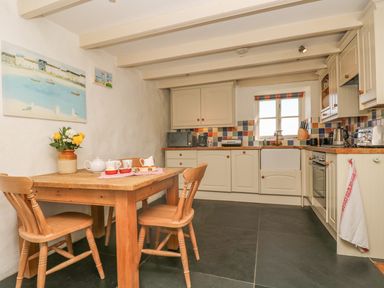 A kitchen with wooden table and chairs beside white cabinets and a window at Boar's House in Penzance