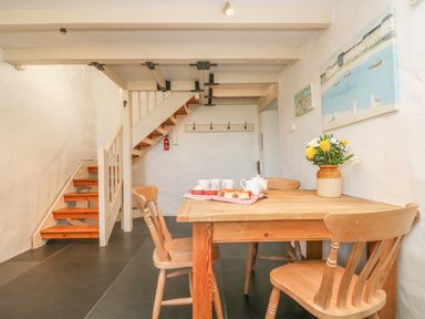 A dining area with a wooden table and chairs near a staircase and paintings on the wall at Boar's House in Penzance