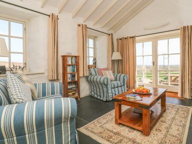 A living room with striped armchairs a wooden coffee table and a bookshelf at Boar's House in Penzance