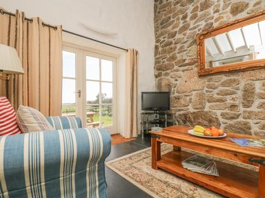 A living room with a striped sofa a wooden coffee table with fruit a TV on a stand and glass doors leading outside at Boar's House in Penzance