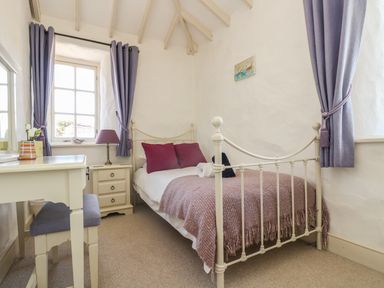 A small bedroom with a white metal bed a desk and a window with purple curtains at Boar's House in Penzance