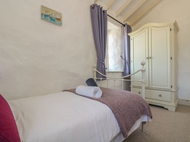 A bedroom with a single bed a rolled towel a white wardrobe and purple curtains at Boar's House in Penzance