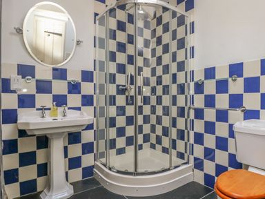 A bathroom with a corner shower, pedestal sink with mirror, and toilet with wooden seat at Boar's House in Penzance
