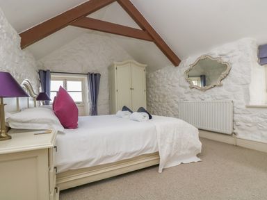 A bedroom with a double bed bedside table wardrobe mirror and exposed wooden ceiling beam at Boar's House in Penzance