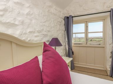 A bedroom with a cream headboard magenta pillows a purple lamp gray curtains and a window showing a countryside view at Boar's House in Penzance