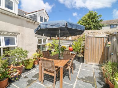 An outdoor patio with wooden table and chairs under a blue umbrella surrounded by potted plants at Ebenezer Cottage in Marazion