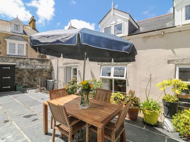 A patio with a wooden table and chairs under a large umbrella and potted plants at Ebenezer Cottage in Marazion