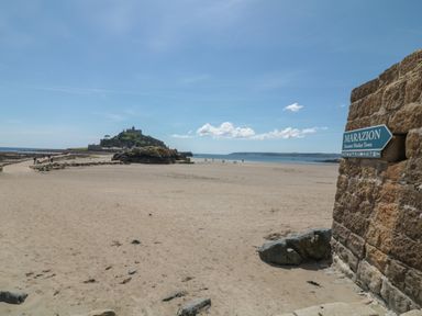A sandy beach with a rocky island and a sign pointing to Marazion at Ebenezer Cottage in Marazion