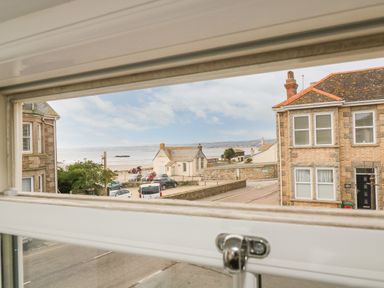 A street view through a window showing parked cars buildings and a beach in the distance at Ebenezer Cottage in Marazion