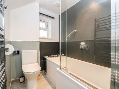 A bathroom with a toilet bathtub shower glass screen and towel rail at Ebenezer Cottage in Marazion