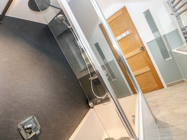 A bathroom with a bathtub shower combination and a wooden door at Ebenezer Cottage in Marazion