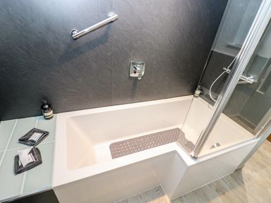 A bathtub with a glass shower screen and bath mat in a bathroom at Ebenezer Cottage in Marazion