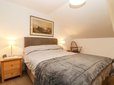 A bedroom with a double bed and two bedside tables each with a lamp and a chair with a pillow at Ebenezer Cottage in Marazion