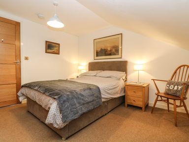 A bedroom with a double bed side tables lamps a wooden chair with cosi pillow and paintings on the wall at Ebenezer Cottage in Marazion