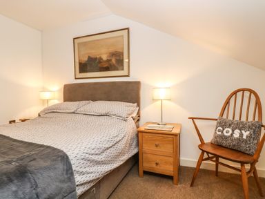 A bedroom with a bed bedside tables with lamps a wooden chair with a cushion and a framed picture on the wall at Ebenezer Cottage in Marazion