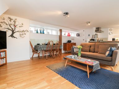 An open living and dining area with a brown sofa and wooden dining table at Ebenezer Cottage in Marazion
