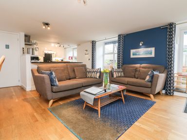 A living room with two brown sofas a coffee table with flowers and books and a blue accent wall at Ebenezer Cottage in Marazion