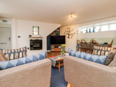 A living room with two brown sofas facing a flat screen TV and a dining table with chairs at Ebenezer Cottage in Marazion