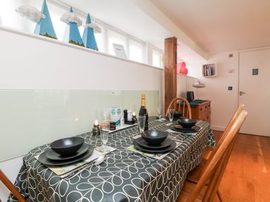 A dining area with a table set for four with black bowls and plates and a bottle on a patterned tablecloth at Ebenezer Cottage in Marazion