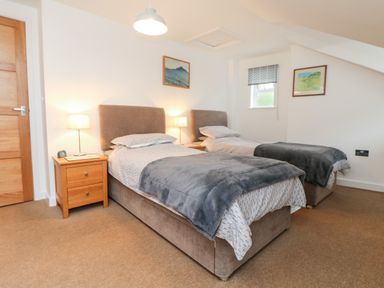 A bedroom with two single beds bedside tables lamps and framed pictures at Ebenezer Cottage in Marazion