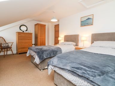 A bedroom with two single beds bedside tables lamps wooden chest of drawers wardrobe and chair at Ebenezer Cottage in Marazion