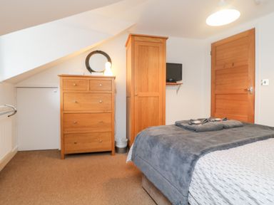 A bedroom with a wooden dresser, wooden wardrobe, wall-mounted TV, and bed with gray blanket at Ebenezer Cottage in Marazion