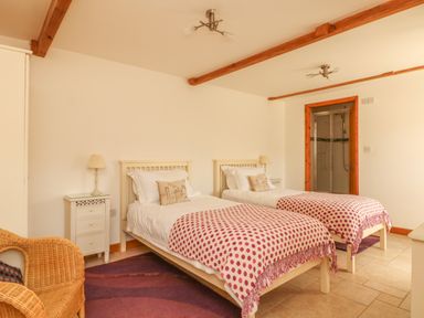 A bedroom with two single beds dressed with polka dot blankets and a wicker chair at Back Of Beyond in St Ives