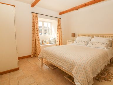 A bedroom with a double bed bedside table lamp window with curtains and cushions at Back Of Beyond in St Ives