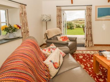 A living room with gray sofas floral cushions and a patterned rug with an open door leading to a garden at Back Of Beyond in St Ives