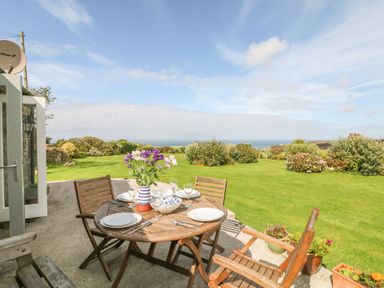 A wooden table with plates and flowers on a patio overlooking a garden and sea at Back Of Beyond in St Ives