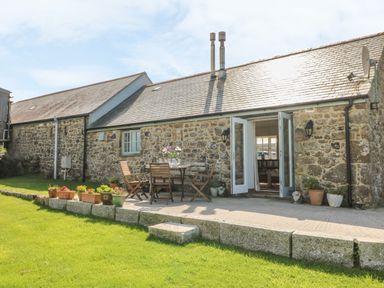 An outdoor patio with wooden chairs and a table with flowers outside a stone cottage at Back Of Beyond in St Ives