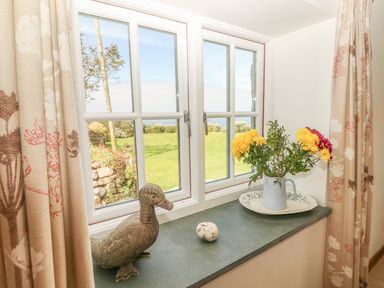 A window with floral curtains and a windowsill with a duck sculpture a small decorative egg and flowers in a jug at Back Of Beyond in St Ives