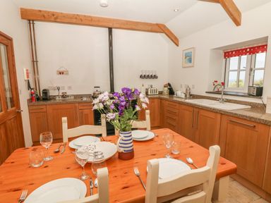 A kitchen with wooden cabinets a dining table set with plates glasses and a vase of flowers at Back Of Beyond in St Ives